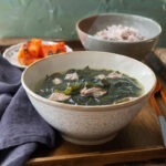 A bowl of beef seaweed soup is served with rice and kimchi on the side.