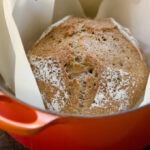 A loaf of no-knead bran bread is baked in a dutch oven.