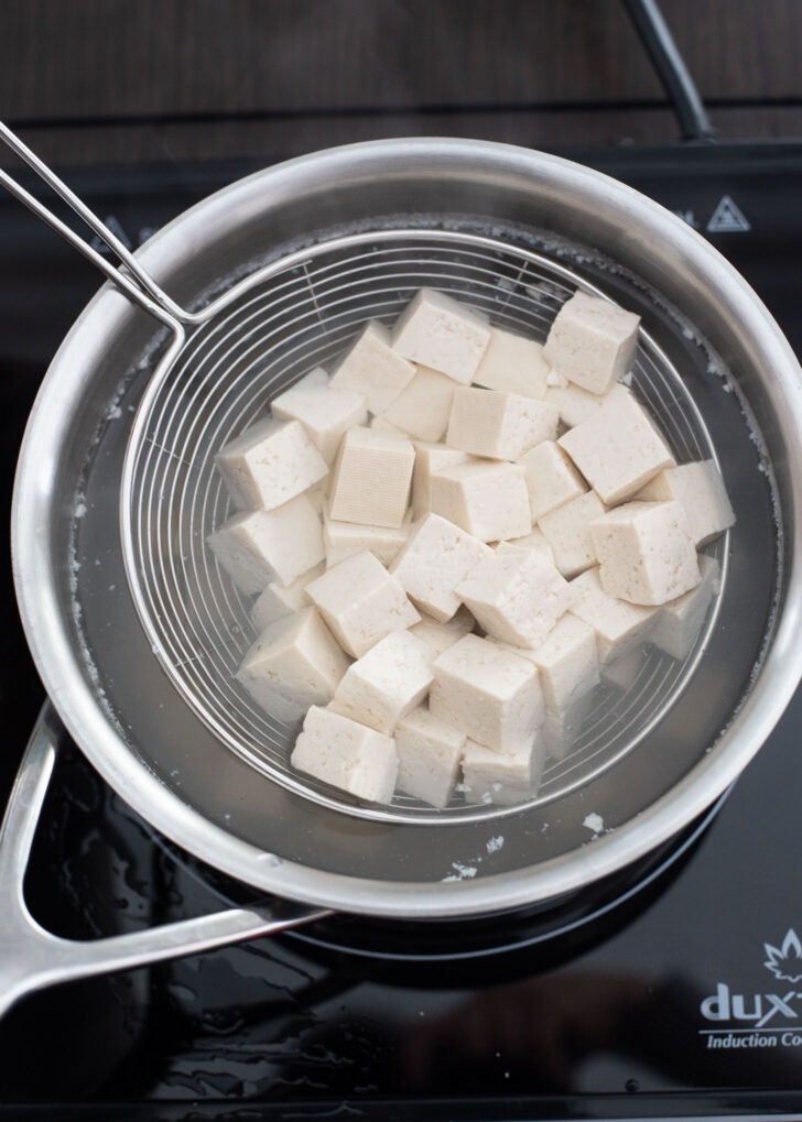 A strainer taking the boiled tofu cubes out of pot.