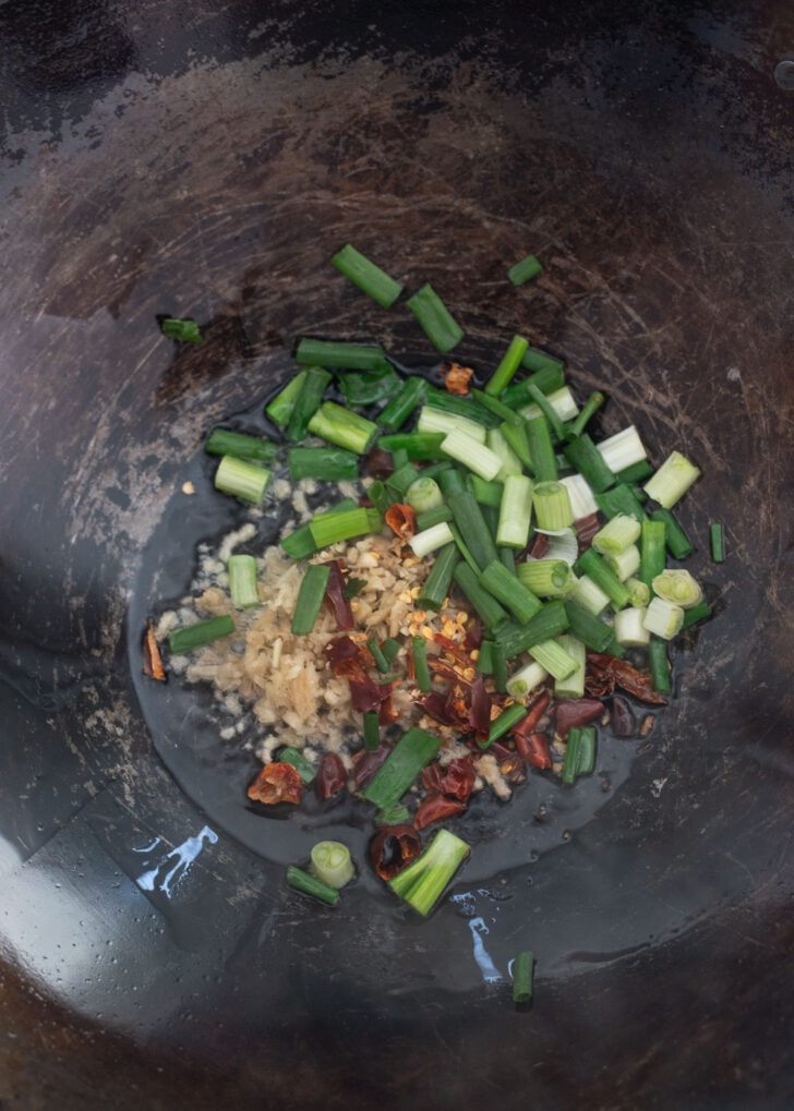 Green onion, ginger, garlic, dried chili are frying in a wok.