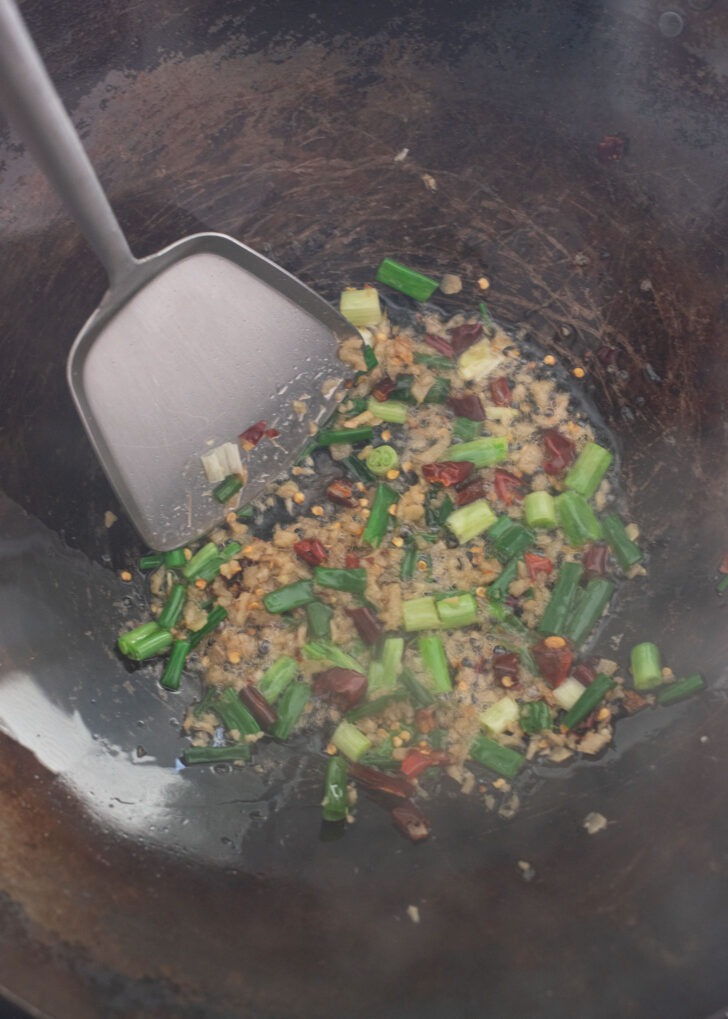 The aromatics ingredients of mapo tofu being stir-fried in a wok.