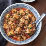 Mapo tofu is dished in a blue bowl with a spoon.