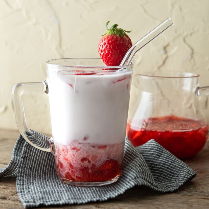 Korean strawberry milk has fresh strawberry syrup is in a glass cup garnished with a piece of strawberry.