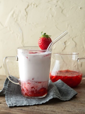 Korean strawberry milk has fresh strawberry syrup is in a glass cup garnished with a piece of strawberry.