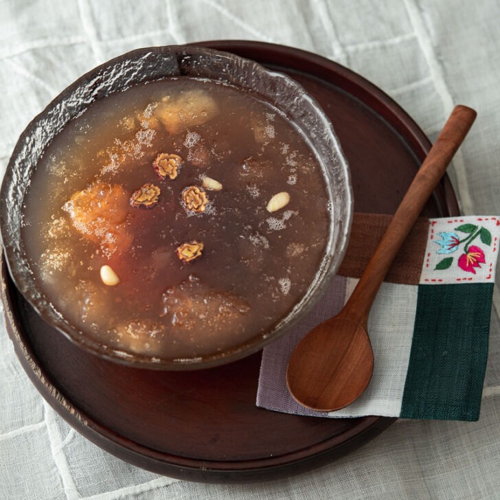 Cold Korean cinnamon punch (sujeonggwa) is served in a glass bowl with a spoon on the side.