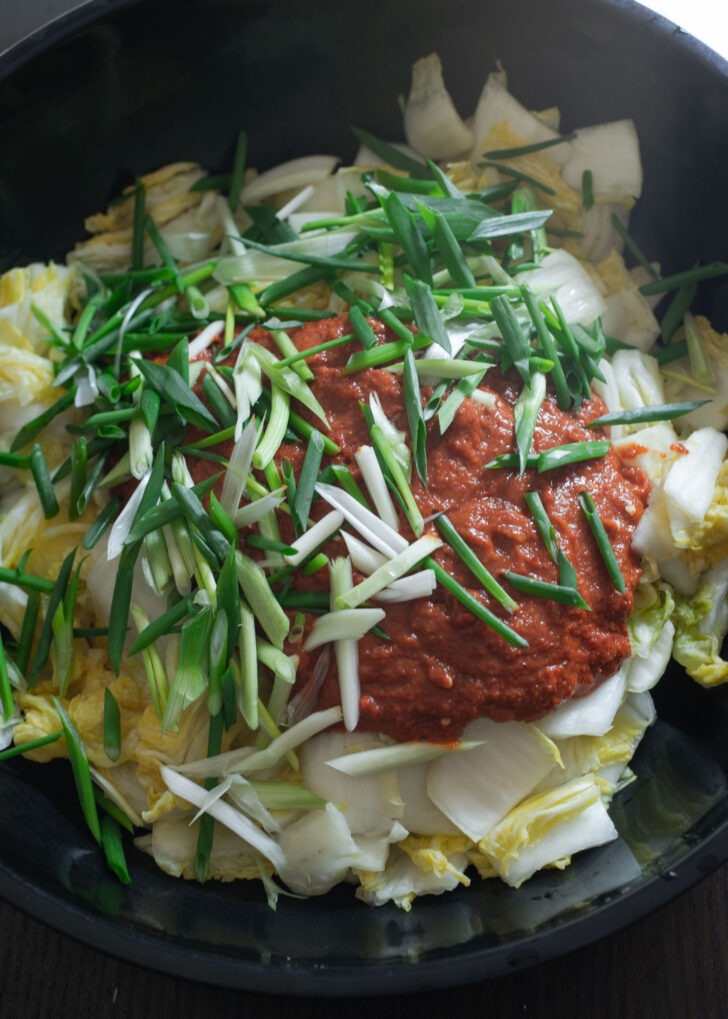 Kimchi paste and green onions are combined with drained cabbage to make vegan kimchi in a large mixing bowl.