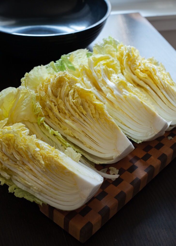 A whole napa cabbage is quartered on a cutting board.
