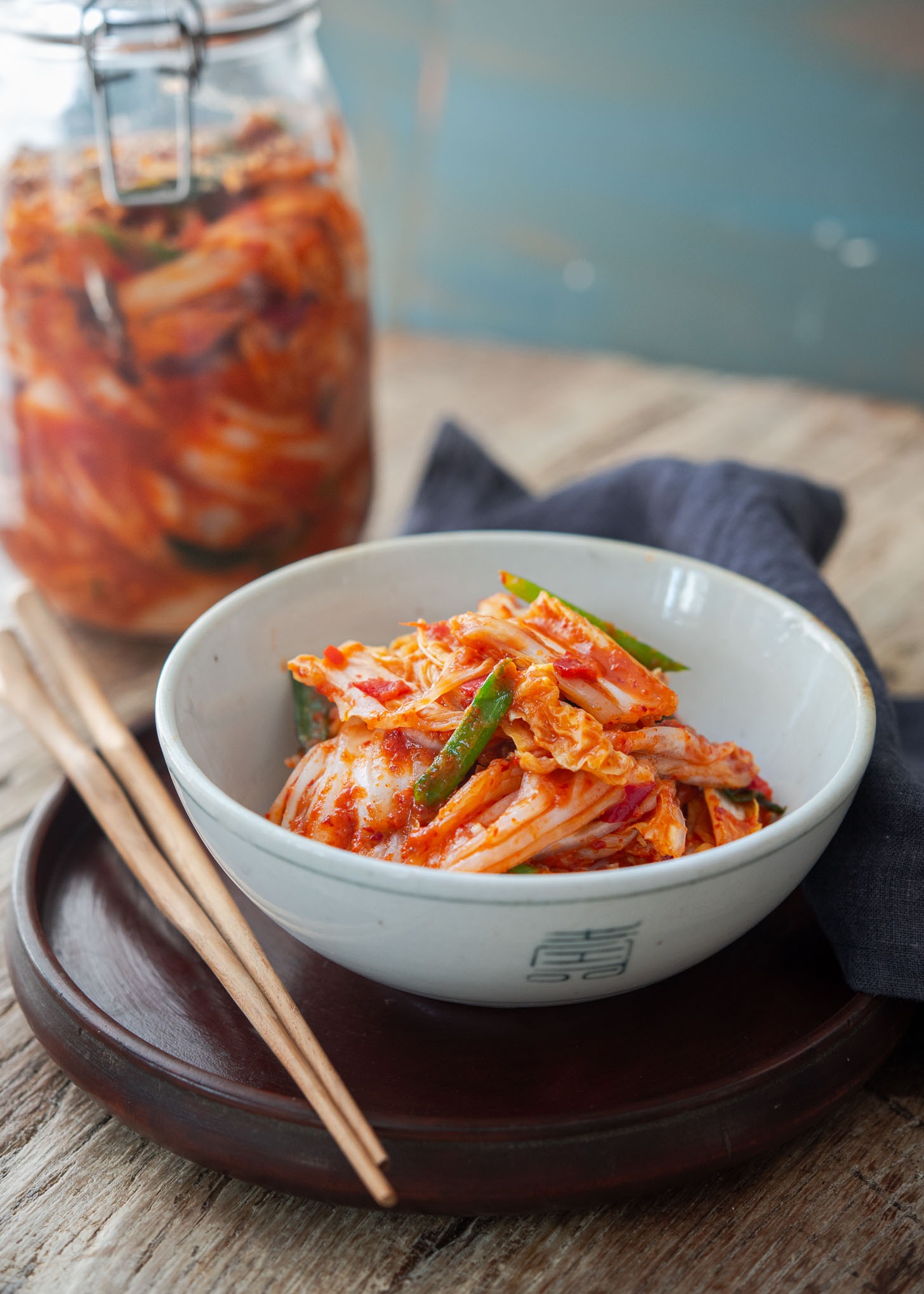 A bowl of freshly made vegan kimchi is placed on a round tray with wooden chopsticks.