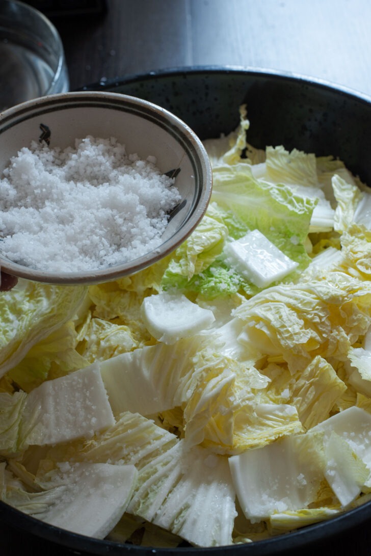 Korean coarse sea salt is sprinkled over cabbage pieces ina large bowl.