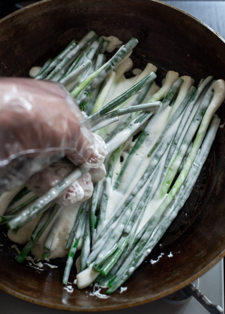Scallions coated with Pajeon batter are added to the hot skillet.