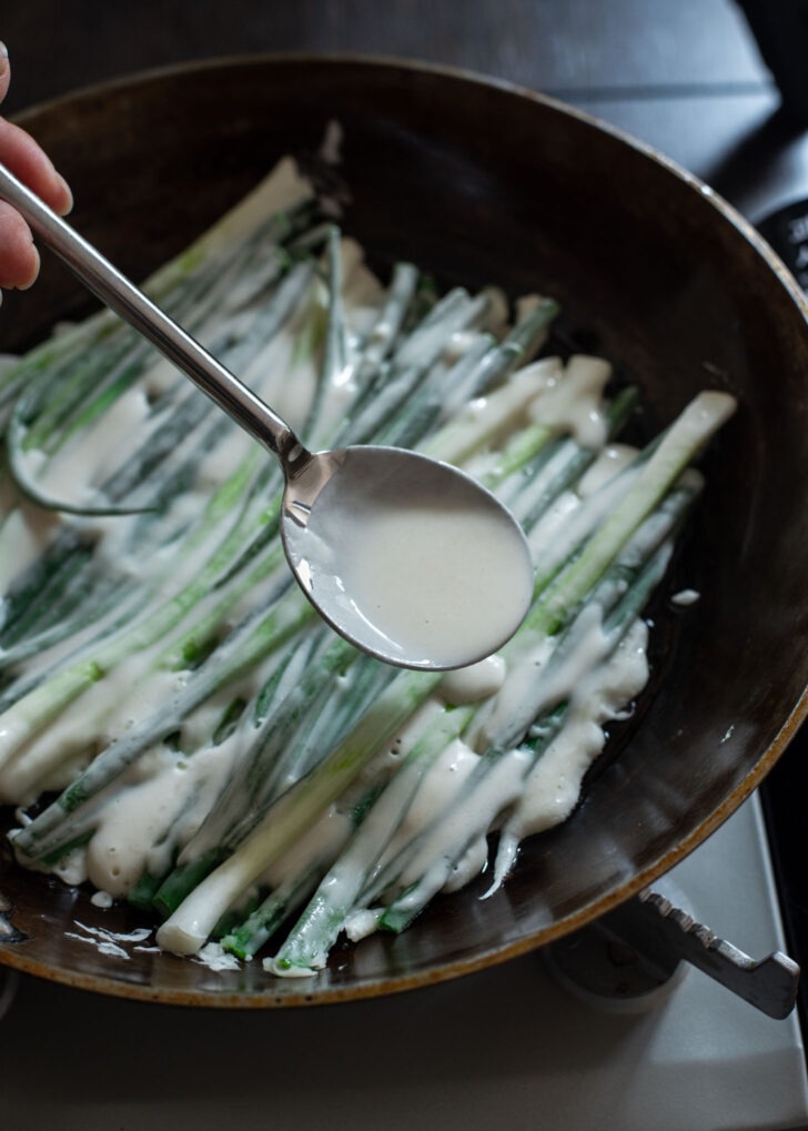 A spoonful of pajeon batter applying to the gap between the scallions.