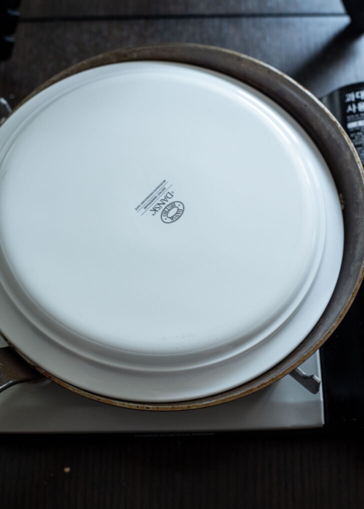 A plate is placed on top of skillet to flip the pancake.