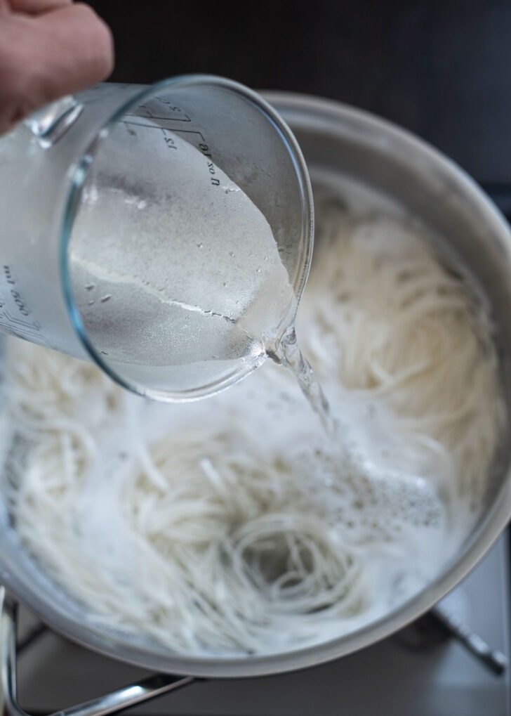 Cold water is added to boiling noodles in a pot.
