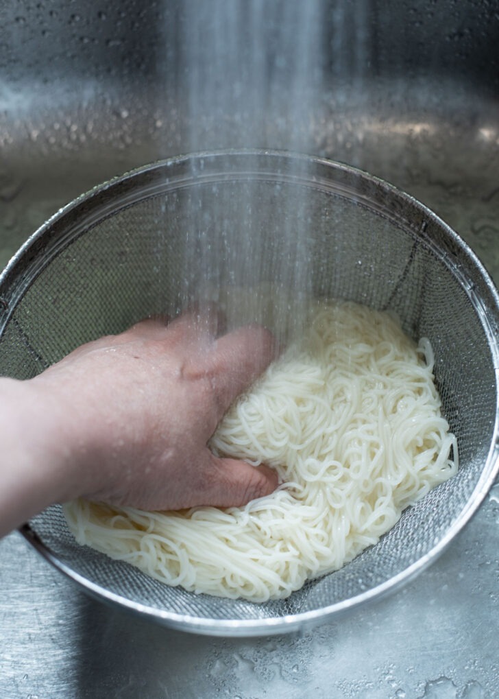 Cooked noodles are being rinsed under running water.
