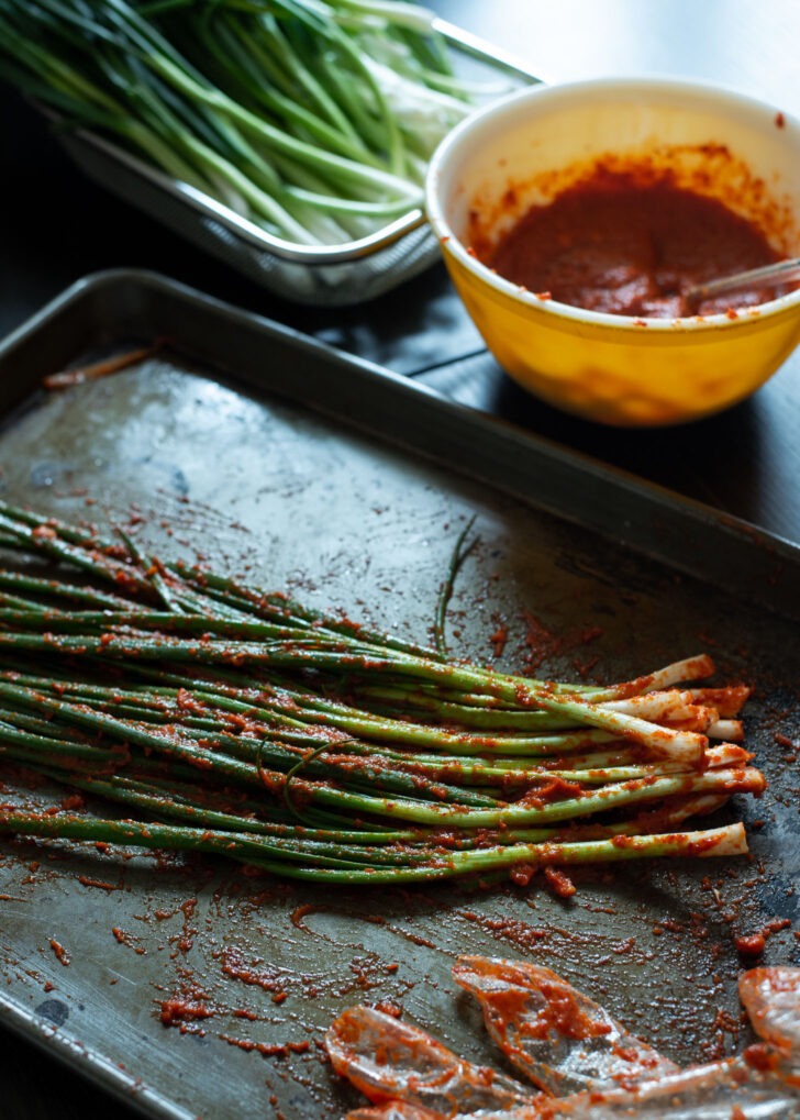 Pa kimchi seasonin paste is applied to the green onion on a baking sheet.