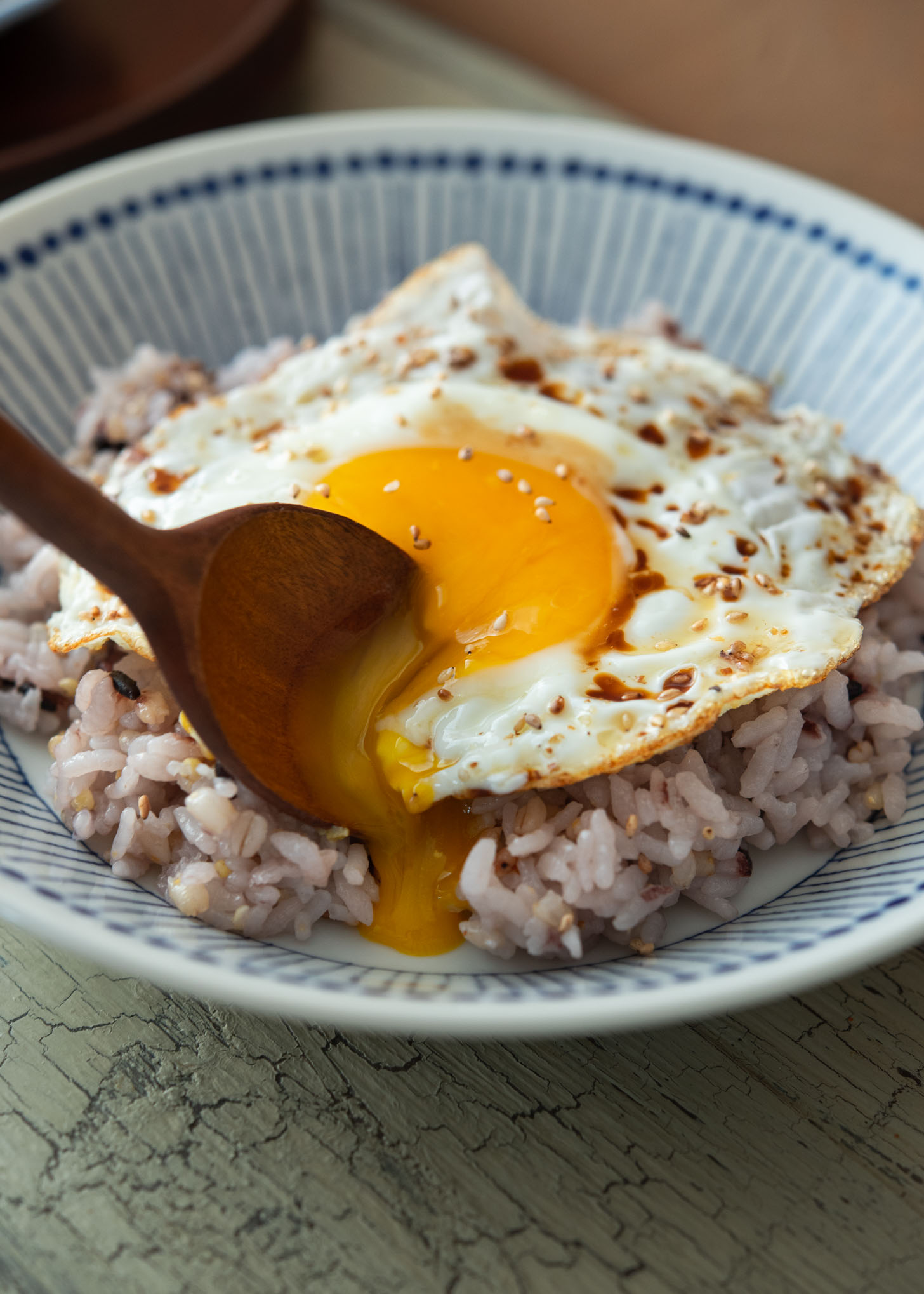 A spoon is breaking the egg yolk of gyeran bap (Korean rice and egg).