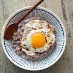 A bowl of gyeran bap is garnished with sesame seeds and served with a spoon.