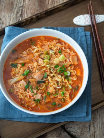 A bowl of kimchi ramen is served on a tray with a pair of chopsticks on the side.