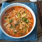 A bowl of kimchi ramen is served on a tray with a pair of chopsticks on the side.