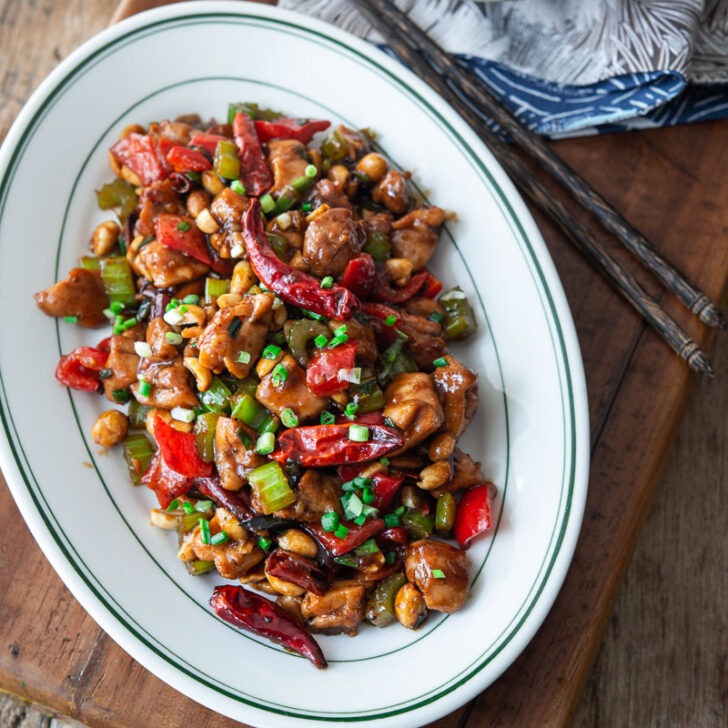 Kung pao chicken is served on a platter with a bowl of rice on the side.