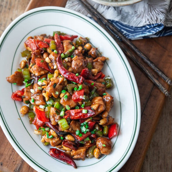 Kung pao chicken is served on a platter with a bowl of rice on the side.