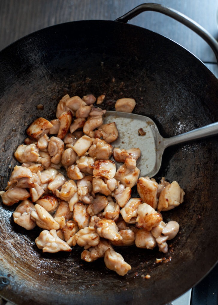 Marinated chicken thigh pieces being stir-fried in a wok.