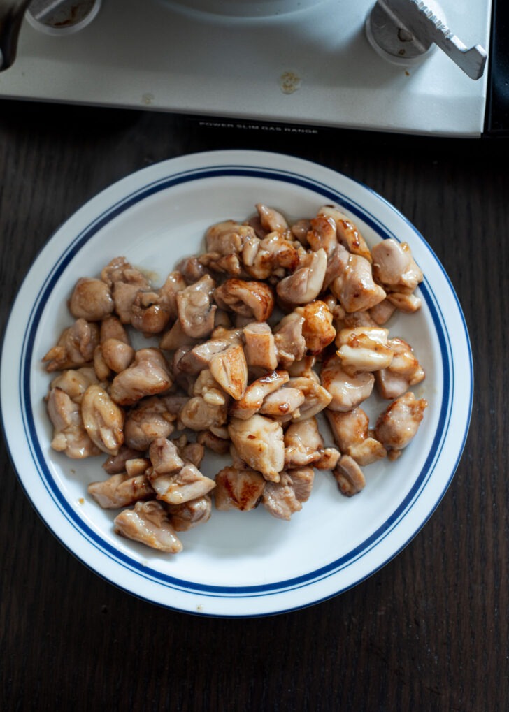 Stir-fried chicken pieces are transferred to a plate.