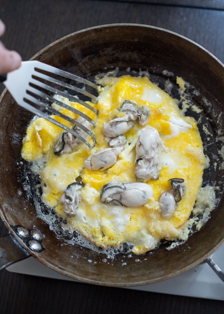 A spatula scrambling the eggs with oysters.