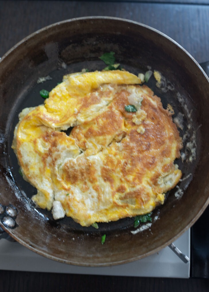 Oyster omelette being flipped to the other side in a skillet.