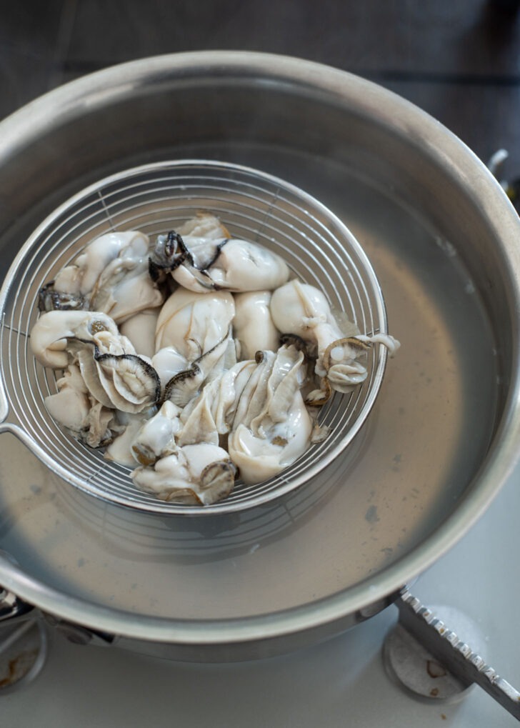 A mesh strainers taking parboiled oysters out of pot.