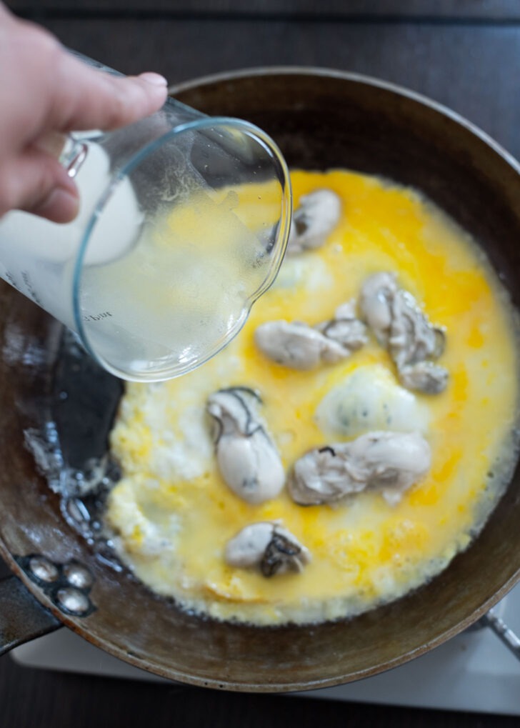 Potato starch batter being poured on egg and oyster mixture.