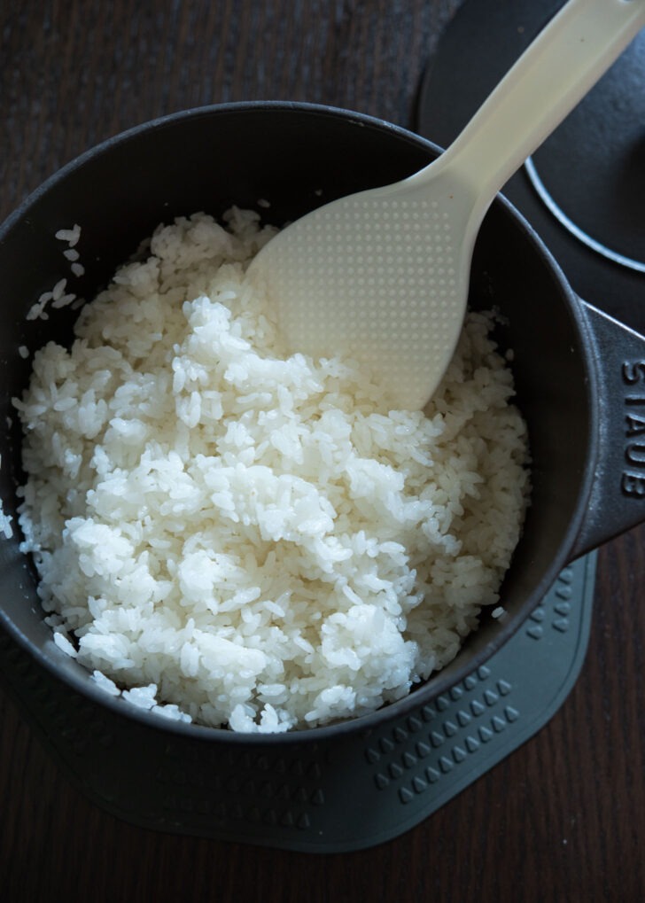 A rice paddle fluffing the cooked Korean rice (white short grain rice) in a pot.