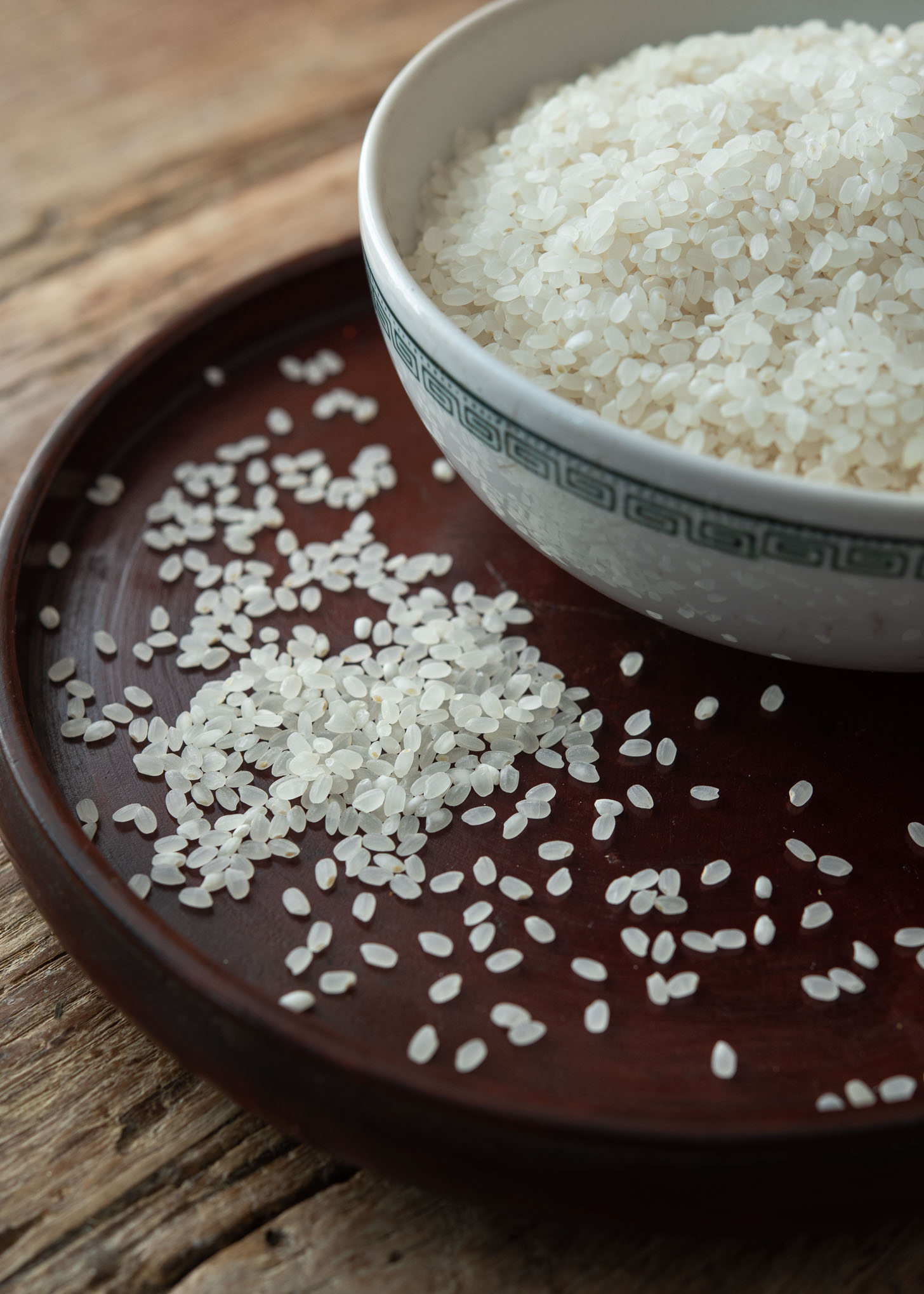 A bowl of short grain rice (Korean rice) next to the scattered white rice grains.