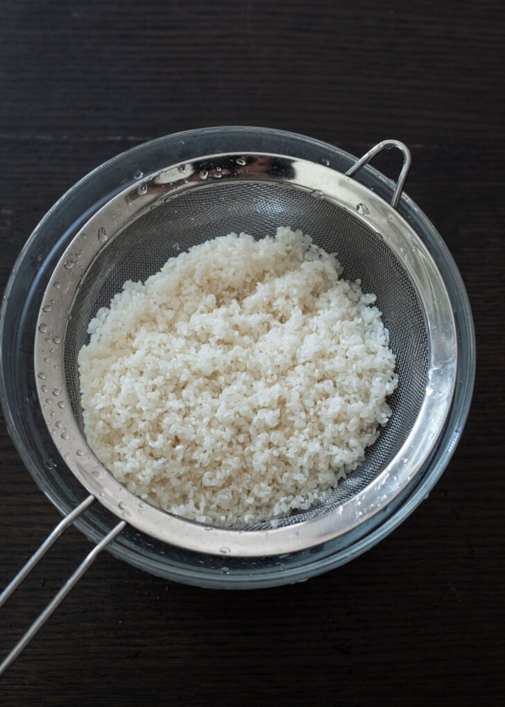 Rinsed Korean rice (short grain rice) strained in a fine mesh strainer.