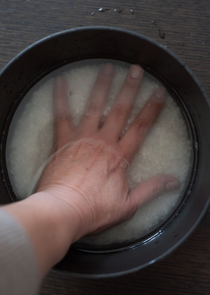 A hand placed on top of rice with water in a pot