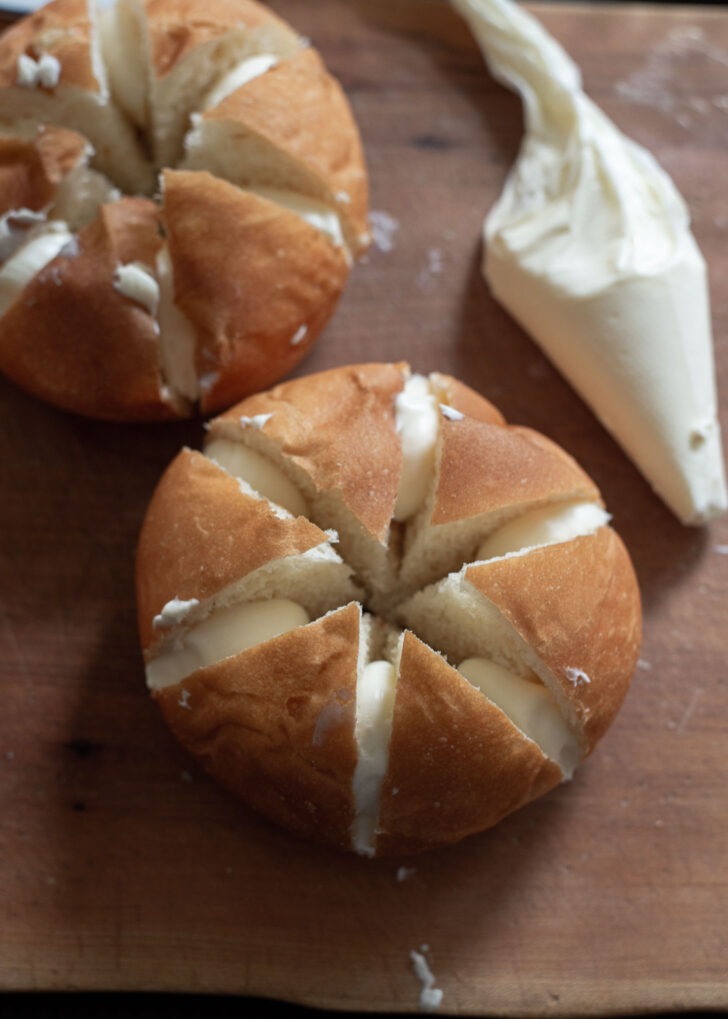 Cream cheese filling is inserted to the scored cracks of the bread rolls.