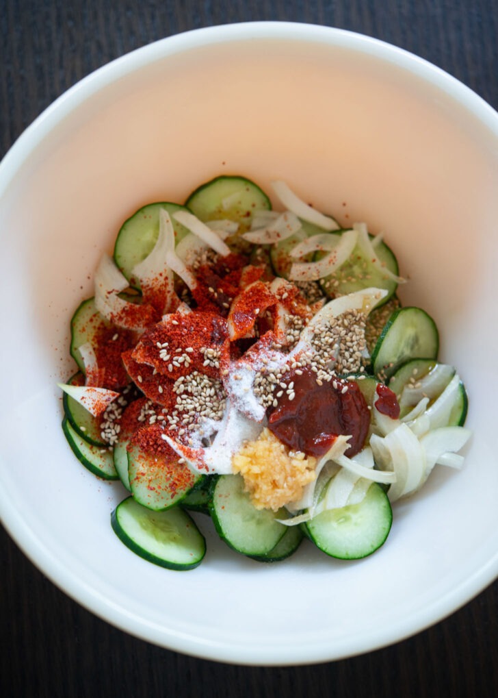 Korean cucumber salad dressing ingredients are added to cucumber slices.