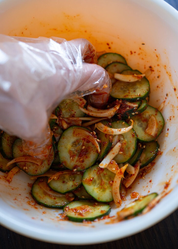 A hand tossing Korean cucumber salad side dish in a bowl.