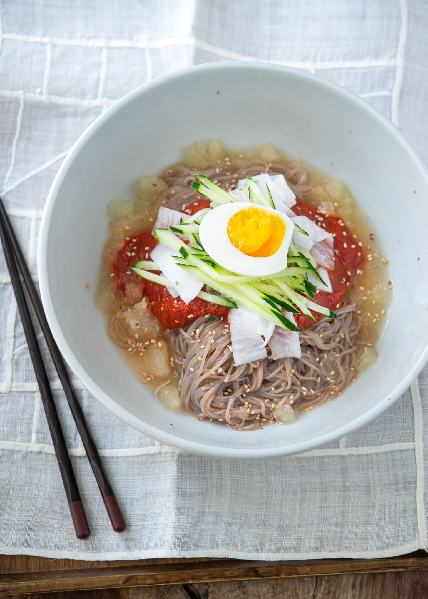 Bibim naengmyeon (spicy cold noodles) garnished with toppings and beef broth in a bowl.