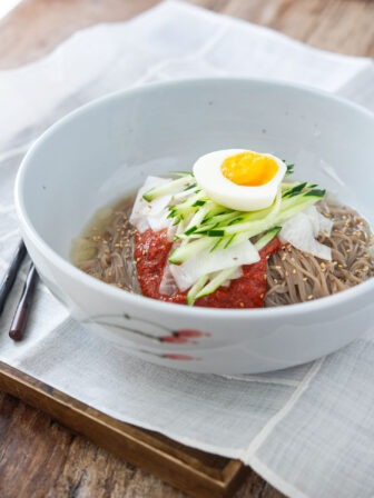 Naengmyeon garnished with bibim naengmyeon sauce and toppings in a bowl.