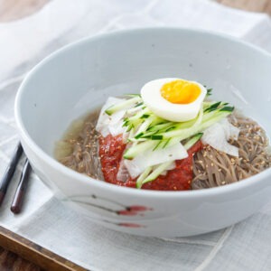 Bibim naengmyeon garnished with bibim naengmyeon sauce and toppings in a bowl.