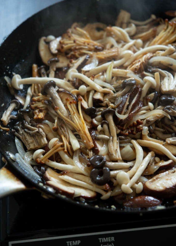 Stir-frying mushrooms in a skillet with the sauce.