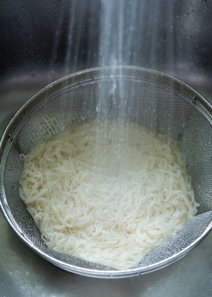 Cooked whet noodles (somyeon) are being rinsed under the cold water.