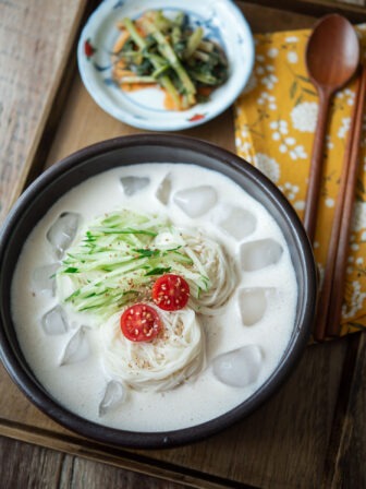 A bowl of kongguksu, Korean cold soy milk noodle soup is garnished with cucumber and tomato.