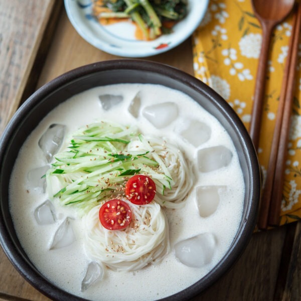 A bowl of kongguksu, Korean cold soy milk noodle soup is garnished with cucumber and tomato.