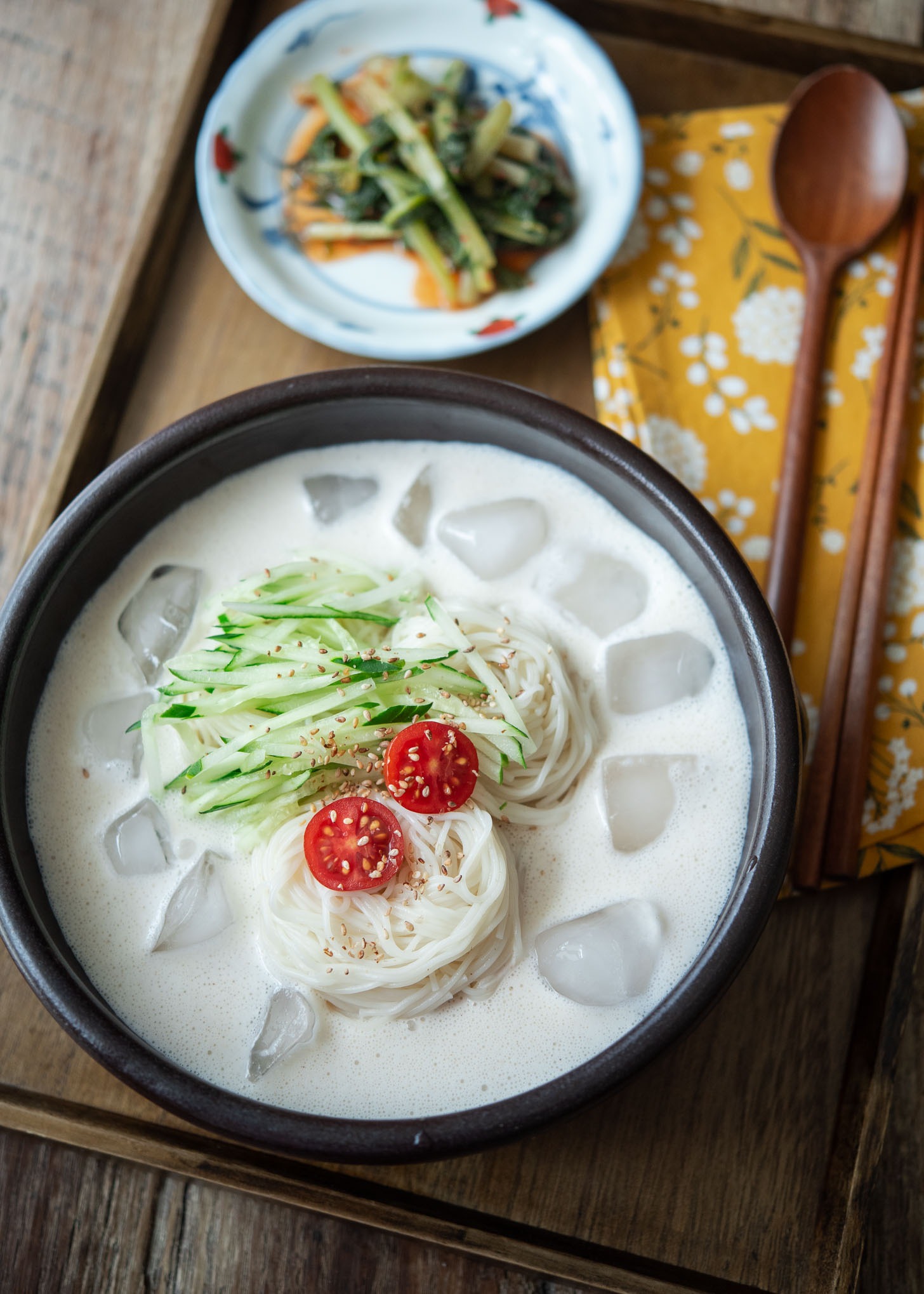 A bowl of kongguksu, Korean cold soy milk noodle soup is garnished with cucumber and tomato.