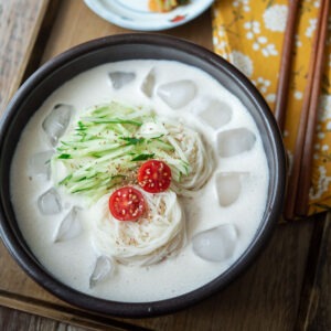 A bowl of kongguksu, Korean cold soy milk noodle soup is garnished with cucumber and tomato.