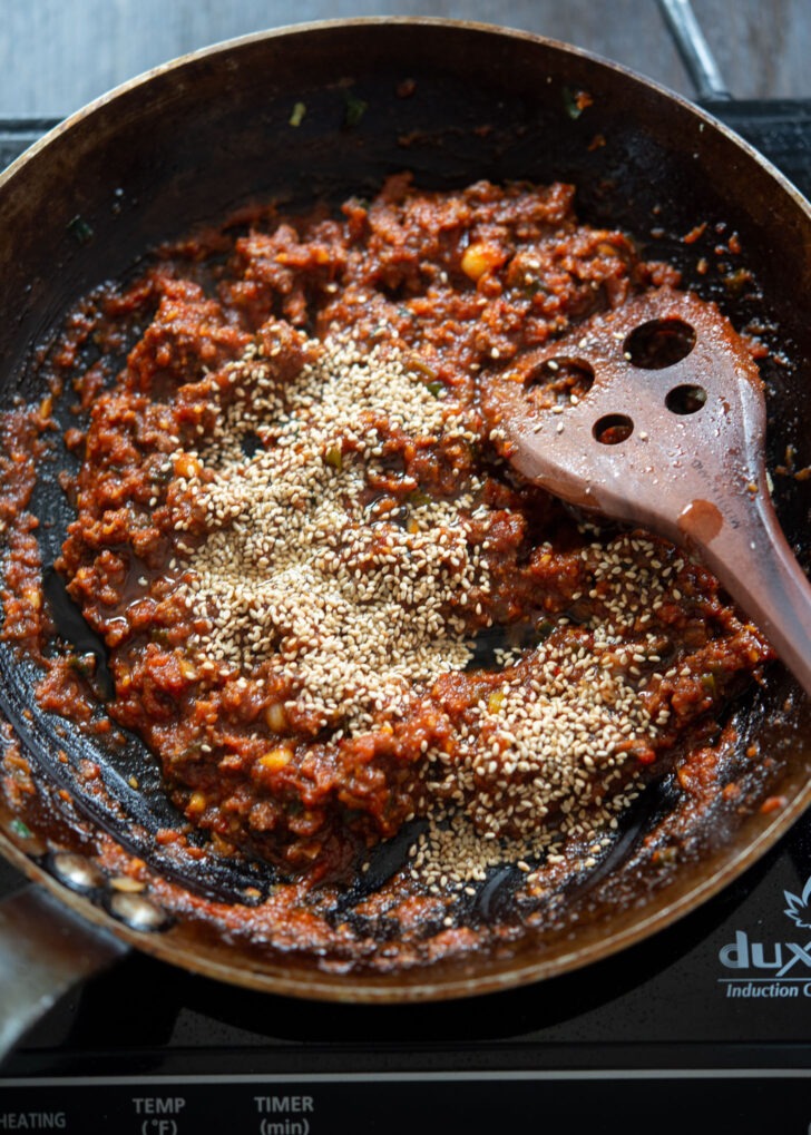 Sesame oil and sesame seeds are added to beef gochujang noodle sauce in a skillet
