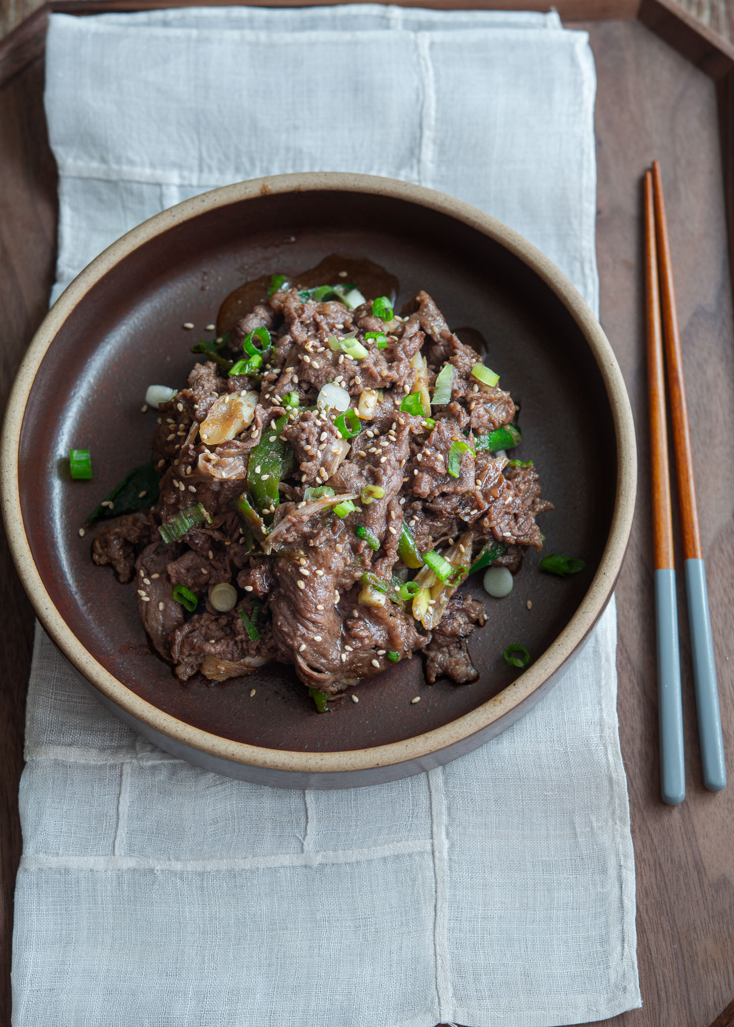 Korean beef bulgogi is served in a dish garnished with sesame seeds and green onion.