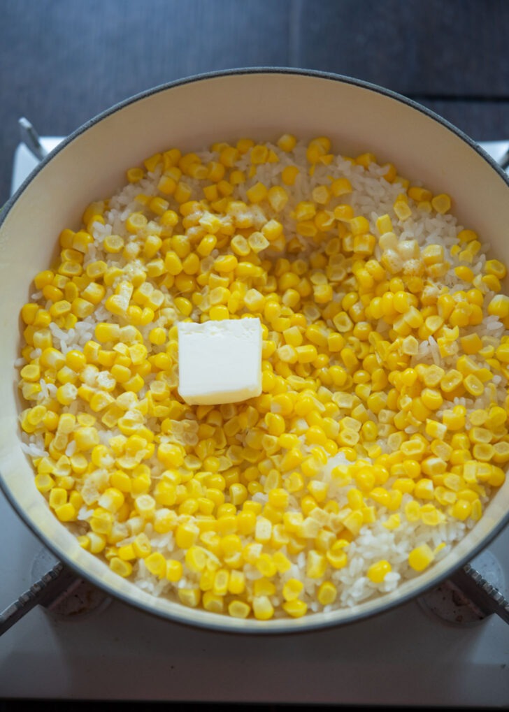 A slice of butter added to corn rice in a pot.